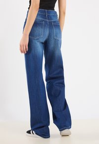 Jean en denim bleu foncé avec une coupe large, dotés de poches arrière et d'une finition délavée. Associés à un haut noir et des chaussures décontractées.