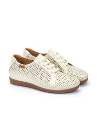 Las zapatillas blancas de cuero presentan patrones florales perforados, acentos beiges y una suela de goma marrón. Diseñadas con cierre de cordones y detalles cosidos.