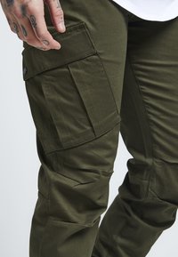 Olijfgroene cargobroek met meerdere zakken, voorzien van een textuurstof, slank model en verstevigde knieën voor duurzaamheid.
