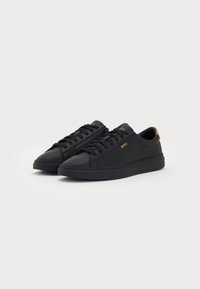 Black low-top sneakers with lace-up design, BOSS logo in gold on side, and brown pull tab at heel on plain white background.