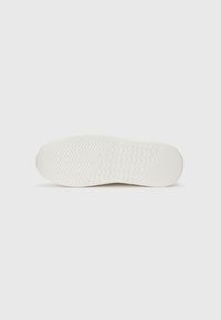 White sneaker outsole with textured herringbone and circular patterns. Features a smooth surface and slight elevation on the heel.