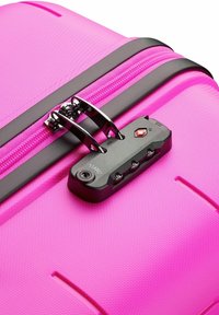Valise rigide rose avec une surface texturée, fermeture éclair noire et serrure à combinaison intégrée avec quatre boutons.