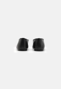 Stivali alla caviglia in pelle nera con una texture liscia, punta rotonda e design minimalista. Presentano cuciture sottili e una suola a profilo basso.
