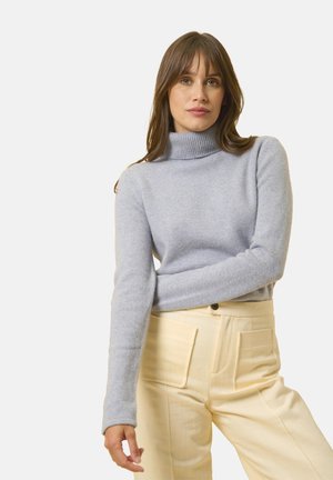Maglione azzurro chiaro a collo alto, con texture lavorata a maglia e maniche lunghe, abbinato a pantaloni crema a vita alta con due tasche frontali.