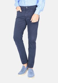 Chino in cotone blu navy con vestibilità slim, con dettagli di cucitura diagonale e tasche frontali, abbinati a mocassini azzurri.