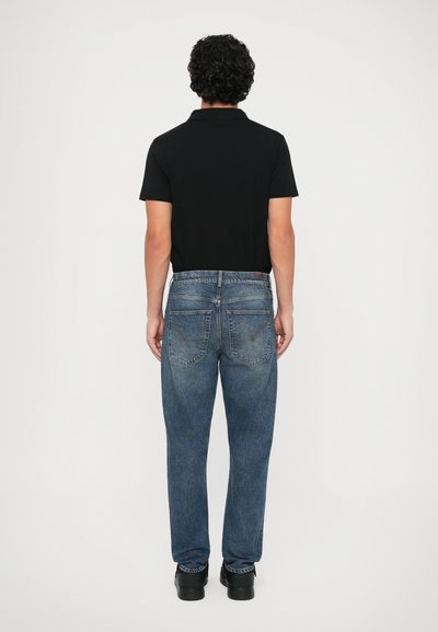 Polo shirt nera, jeans in denim blu, vestibilità comoda, lavaggio medio, due tasche posteriori con cuciture a contrasto, abbinati a scarpe nere.