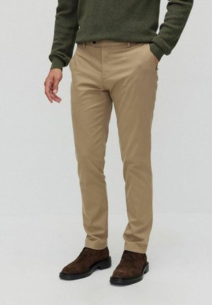 Beiga bomullsshorts i slim fit, med bälteshällor och sidofickor, kombinerade med en strukturerad grön tröja och bruna mockaskor.