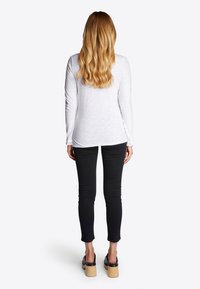 Blusa blanca de manga larga con un corte holgado, combinada con jeans de tiro bajo negros y zapatos de plataforma negros. Cabello suelto en ondas.