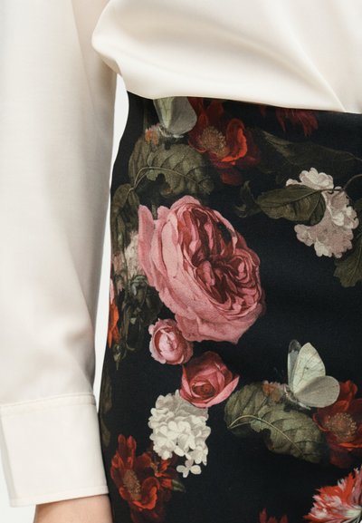 Fehér hosszú ujjú blúz, ami be van tűrve egy fekete szoknyába, amely részletes virág- és pillangómintával díszített rózsaszín, piros, fehér és zöld árnyalatokban.