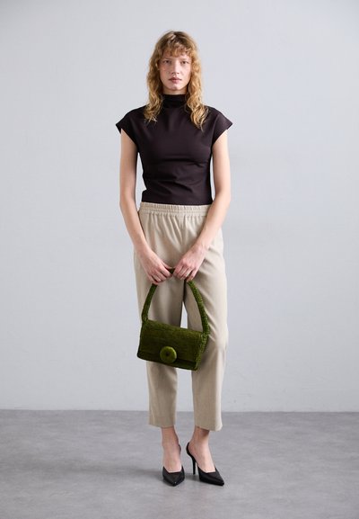 Brun fitted top, beige tapered bukser, sorte stiletto hæle og en grøn vævet håndtaske med et cirkulært detalje. Minimalistisk, moderne outfit.
