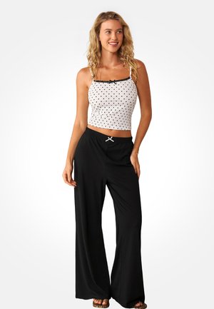 Witte crop top met zwarte polkadots, afgezet met zwart kant en een strik; gecombineerd met zwarte wijde broekspijpen met trekkoord en accentnaden.