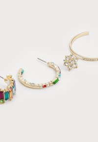 Three pairs of hoop earrings: one with colorful gems, one with a gold band and accents, and a third with a floral design of clear rhinestones.
