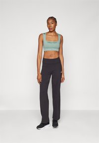 Žalia, trumpa sportinė liemenėlė su logotipo juosta, derinama su juodomis, prigludusiomis kelnėmis. Juodi sportbačiai su baltais padais baigia sportinį įvaizdį.