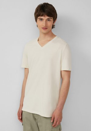 Jasno beżowa koszulka typu V-neck wykonana z miękkiego materiału, z krótkimi rękawami i luźnym krojem. Minimalistyczny design bez wyraźnych wzorów czy logo.