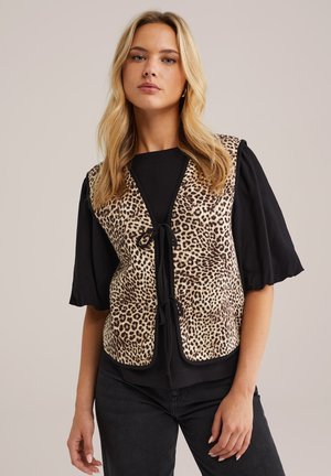 Luipaardprint vest met een geknoopte voorkant, voorzien van een zachte textuur en contrasterende zwarte mouwen. Draagt over een zwart topje, gecombineerd met donkere broeken.