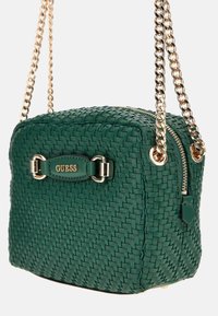Borsa a tracolla intrecciata verde con catena metallica, hardware dorato e chiusura con zip. Presenta un logo distintivo sulla parte anteriore. Forma rettangolare compatta.