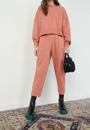 Loungewear sæt i blødt, koralfarvet stof; cropped sweatshirt med oversized ærmer og matchende bukser. Sorte accessories og chunky støvler med grøn sål.