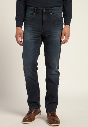 Pantalones vaqueros de denim en azul oscuro con un ligero desgaste, con un diseño clásico de cinco bolsillos, cierre de botón y ajuste entallado, combinados con zapatos de cuero marrón.
