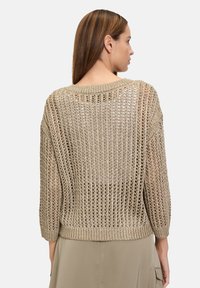 Pull léger en maille ouverte de couleur or métallisé. Il a un col rond, des manches trois-quarts et une coupe décontractée avec un ourlet côtelé.