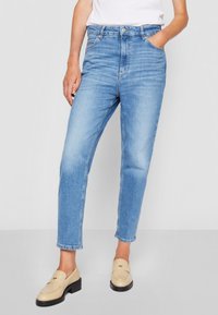 Light blue high-waisted jeans with a straight leg fit, featuring five pockets and stitched detailing. Worn with beige loafers.