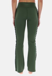 Zielone rozszerzane spodnie o gładkiej fakturze, z czarną falbaniastą lamówką po bokach i wysokim pasem.