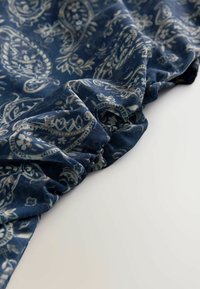 Sinine mustriga kangas paisleymustriga, näidates pehmet tekstuuri ja kortsutatud serva detaile.