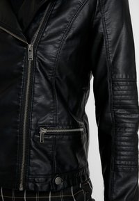 Sort læderjakke med lynlås foran, quiltet detalje på ærmerne og metal hardware accenter. Har en sidelomme med lynlås.