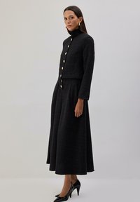 Zwarte jas van een wolmix met een hoge kraag, gouden knopen en een bijpassende lange rok met een uitlopende snit en een gladde textuur.