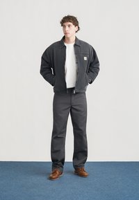 Μαύρο τζιν μπουφάν, λευκό μπλουζάκι, γκρι παντελόνι και καφέ παπούτσια. Το μπουφάν διαθέτει φερμουάρ μπροστά και τσέπη στο στήθος με λεπτομέρεια λογότυπου.