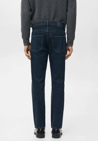 Vaqueros de mezclilla azul oscuro con un diseño de pierna recta, con dos bolsillos traseros y una cintura estándar, combinados con zapatos negros.