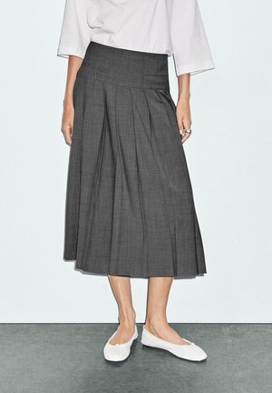 Gonna midi grigia plissettata con vita piatta. Abbinata a scarpe bianche slip-on senza tacco. Tessuto liscio con un motivo sottile.