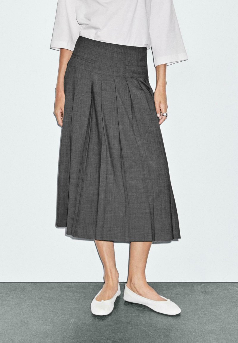 Gonna midi grigia plissettata con vita piatta. Abbinata a scarpe bianche slip-on senza tacco. Tessuto liscio con un motivo sottile.