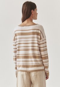 Pull rayé en crème et beige, présentant une coupe ample, un col large et un ourlet côtelé. Tissu doux et texturé avec des rayures horizontales.
