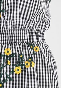 Schwarz-weißes Gingham-Muster mit gelber Floralstickerei. Verfügt über einen gerafften elastischen Bund und eine weiche Textur.