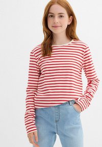 Maglietta a maniche lunghe a righe rosse e bianche con scollatura rotonda, caratterizzata da un fit rilassato e un tessuto morbido, abbinata a jeans azzurri chiari.