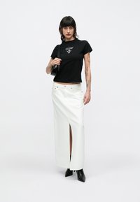 Μαύρο εφαρμοστό μπλουζάκι με λευκό λογότυπο, σε συνδυασμό με μακριά λευκή τζιν φούστα με σκίσιμο στο πλάι και μαύρα μποτάκια αστραγάλου.