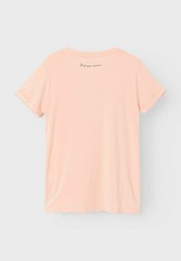 Kortærmet, pastelfarvet lyserød t-shirt med rund hals og oprullede ærmer. Har en diskret trykt sætning på den øverste del af ryggen. Glat tekstur.