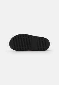 Suela de zapato de goma negra con superficie texturizada; cuenta con estrías y ranuras para mayor agarre; forma redondeada con un borde suave.