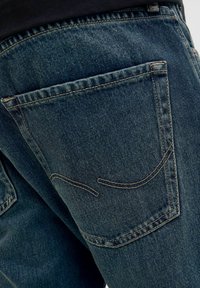 Denim jeans in een donkerblauwe kleur, met zichtbare stiksels en een achterzak met unieke gebogen naden.
