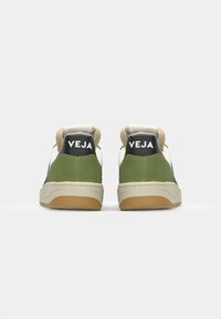 Grønn semsket og svart skinnsneaker med beige mellomsåle og gummisåle. Har polstret krage og hvit merkevarelogo på hælen.