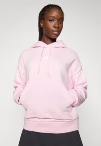 Hoodie rose clair avec une poche avant, capuche à cordon et logo blanc sur la poitrine. Tissu en mélange de coton doux, design décontracté.