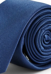 Marineblaue Krawatte mit einem strukturierten diagonalen Muster, eng aufgerollt, die den glatten Stoff und die präzisen Nähte an den Kanten zeigt.