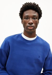 Blaues Baumwollsweatshirt mit Rundhalsausschnitt, langen Ärmeln und kleinem gesticktem Logo auf der Brust. Glatte Textur in einfarbiger Ausführung.