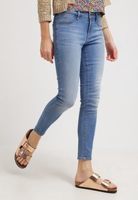 Ljust tvättade skinny jeans med slim fit, med en midjehöjd och kontrasterande sömmar, i kombination med metalliska slip-on sandaler.