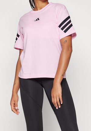 Personne portant un t-shirt rose clair avec des bandes noires sur les manches et un logo, associé à des leggings de sport noirs ajustés.