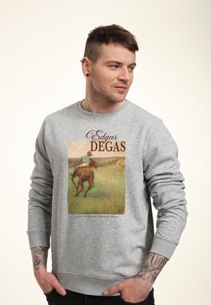 Man draagt grijze sweater met afbeelding van een schilderij van Edgar Degas, met een jockey in het blauw op een kastanjebruine paard in een grasveld.