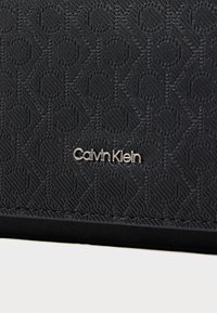 Zwarte portemonnee van Calvin Klein met een gestructureerd patroon van in elkaar grijpende cirkels, matte afwerking en zilveren logo-accent.