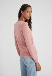 Pull tricot rose clair avec des manches longues, un col rond et un ourlet côtelé. Associé à un jean en denim bleu taille haute.
