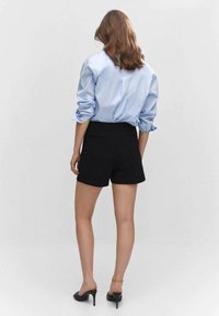 Czarne spodenki o dopasowanym kroju, zestawione z jasnoniebieską koszulą zapinaną na guziki. Koszula ma podwinięte rękawy i gładką teksturę.