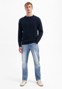 Marineblauwe gebreide trui met een ronde hals en raglanmouwen, gecombineerd met lichtblauwe jeans en witte sneakers. Eenvoudig, casual ontwerp.